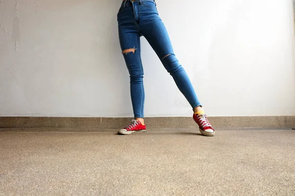 Zapatillas rojas. Piernas de mujer en zapatillas de deporte rojas y pantalones vaqueros azules en el fondo del piso — Foto de Stock