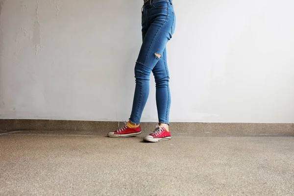 Sapatilhas vermelhas. Pernas femininas em tênis vermelhos e jeans azuis no chão de fundo — Fotografia de Stock