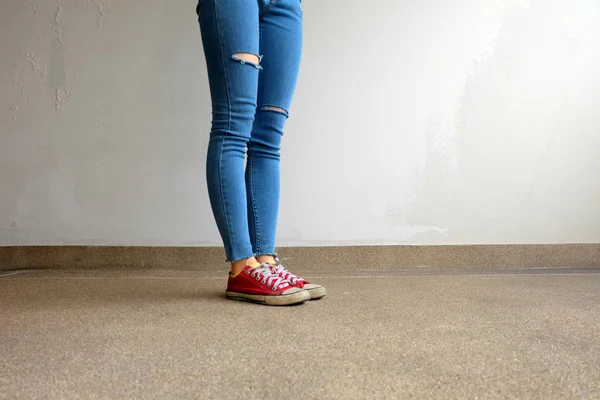 Zapatillas rojas. Piernas de mujer en zapatillas de deporte rojas y pantalones vaqueros azules en el fondo del piso —  Fotos de Stock