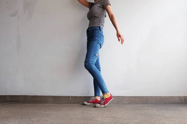 Zapatillas rojas. Piernas de mujer en zapatillas de deporte rojas y pantalones vaqueros azules en el fondo del piso — Foto de Stock