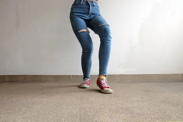 Zapatillas rojas. Piernas de mujer en zapatillas de deporte rojas y pantalones vaqueros azules en el fondo del piso — Foto de Stock