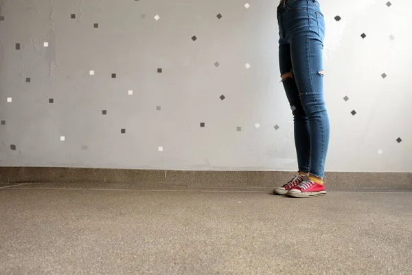 Röda Sneakers. Kvinnans ben i röda Sneakers och blå Jeans på golvet bakgrund — Stockfoto