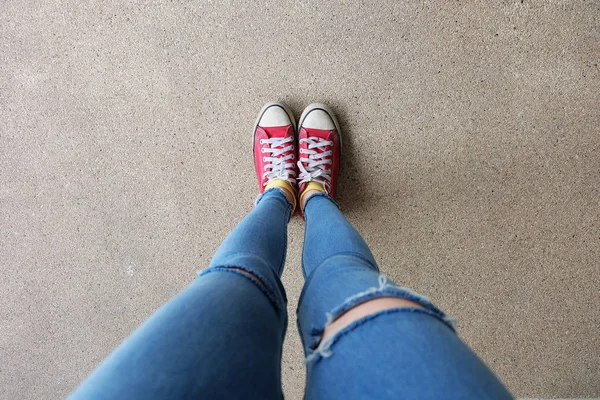 Close-up van rode Sneakers. Selfie Womans benen in rode Sneakers en Blue Jeans op vloer achtergrond — Stockfoto