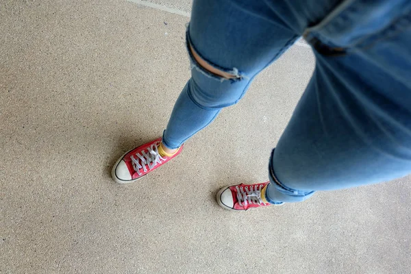 Närbild av röda Sneakers. Selfie kvinnans ben i röda Sneakers och blå Jeans på golvet bakgrund — Stockfoto