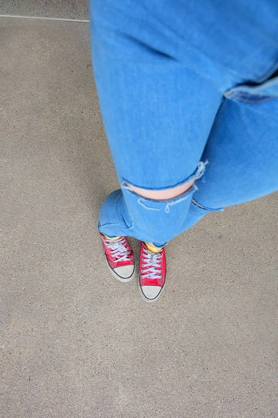 Zapatillas rojas de cerca. Selfie piernas de mujer en zapatillas de deporte rojas y pantalones vaqueros azules en el fondo del piso —  Fotos de Stock