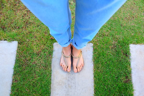 妇女的腿和脚穿在水泥和绿色的草地上的金色凉鞋背景伟大的任何使用 — 图库照片
