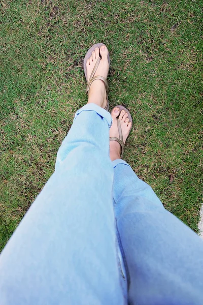 女人的腿和脚在水泥和绿草背景上穿金色凉鞋 — 图库照片