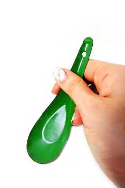 Kadın el manikürlü granit ile bir kaşık tutan çiviler. Beyaz zemin üzerine yeşil çinko kaşık kadar kapatın