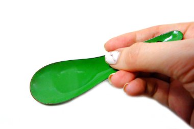 Kadın el manikürlü granit ile bir kaşık tutan çiviler. Beyaz zemin üzerine yeşil çinko kaşık kadar kapatın