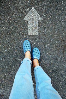 Selfie mavi ayakkabı ve kot. Kadın ayakları ile yol çimento arka plan büyük beyaz ok satırında herhangi bir kullanım için ayakta.