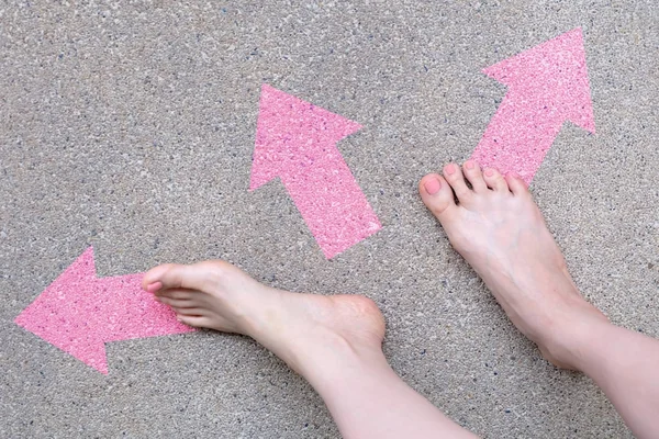 Pink Arrow Choice Concept. Female Bare Feet with Pink Nail Polish Manicure Standing and Many Direction Arrows Choices on the Road Background Great for Any Use.