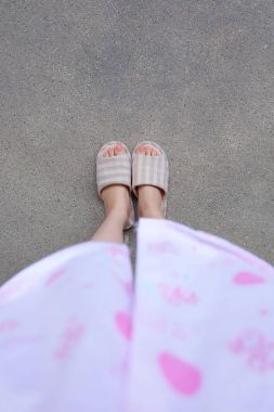 Pembe manikür çivi ile damalı sıcak terlik. Kadın bacaklar ve ayaklar pembe pijama ve terlik çimento arka plan büyük herhangi bir kullanım için üzerinde.