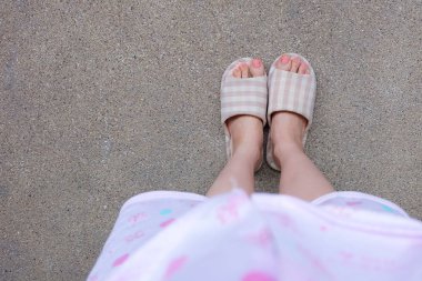 Pembe manikür çivi ile damalı sıcak terlik. Kadın bacaklar ve ayaklar pembe pijama ve terlik çimento arka plan büyük herhangi bir kullanım için üzerinde.