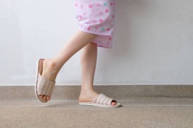 Pembe manikür çivi ile damalı sıcak terlik. Kadın bacaklar ve ayaklar pembe pijama ve terlik çimento arka plan büyük herhangi bir kullanım için üzerinde.