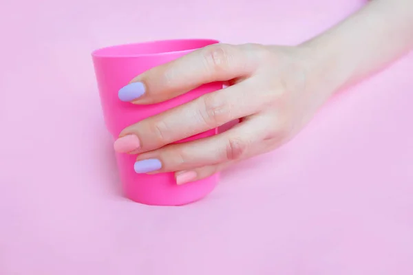 Hand Hold a Glass with Pink Manicure Nails. Woman Hand Holding Pink Plastic Glass of Water on Pink Background Great For Any Use.