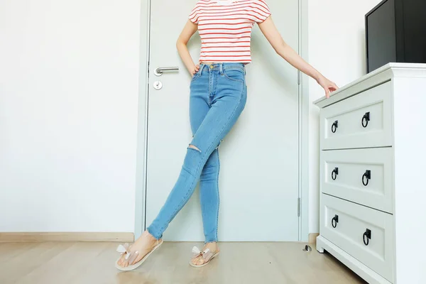 Summer Fashion Nude Bow Sandal (Footwear) and Slim Legs in The Room. Female Sexy Long Legs. Beautiful Slim Legs Woman Standing with Nude Sandals and Lack Blue Jean on Wooden Floor at Home Background