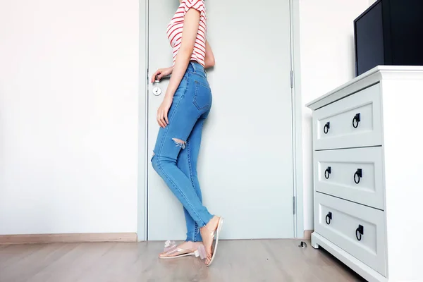 Summer Fashion Nude Bow Sandal (Footwear) and Slim Legs in The Room. Female Sexy Long Legs. Beautiful Slim Legs Woman Standing with Nude Sandals and Lack Blue Jean on Wooden Floor at Home Background