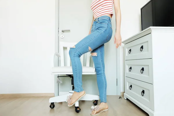 Summer Fashion Nude Bow Sandal (Footwear) and Slim Legs in The Room. Female Sexy Long Legs. Beautiful Slim Legs Woman Standing with Nude Sandals and Lack Blue Jean on Wooden Floor at Home Background