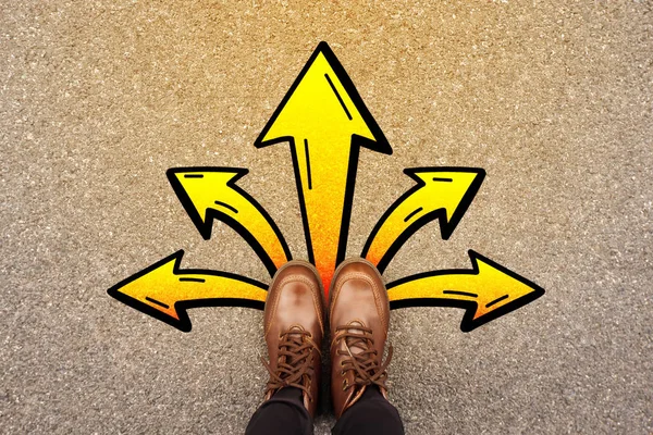Feet and arrows on road background. Top view. Selfie woman in leather ankle boots on pathway with yellow graffiti arrow sign choices. New start and movement idea concept. Hipster brown shoes style.
