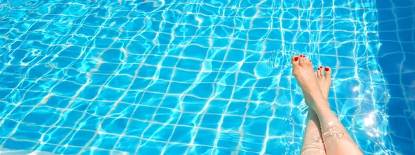 Feet in swimming pool water. Selfie of legs and barefoot with red pedicure and manicure nails on blue sea background. Vacation at summer holiday.