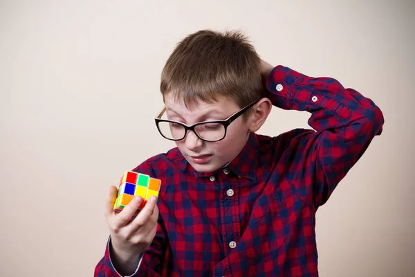 Уверенный в себе улыбающийся маленький мальчик-ботан, держа в руках кубик головоломки. — стоковое фото