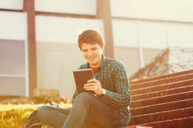 Genç adam tablet merdiven üstünde bir şehirde taping gülümseyen