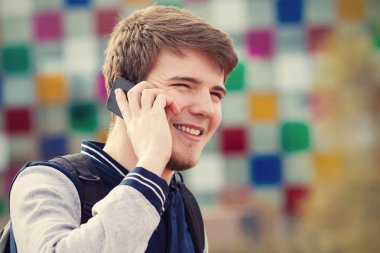 Genç adam bir şehirde cep telefonu konuşurken gülümseyen .