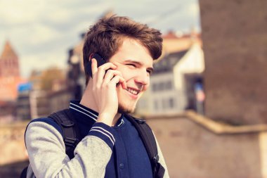 Genç adam bir şehirde cep telefonu konuşurken gülümseyen .