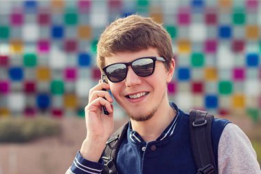 Genç adam bir şehirde cep telefonu konuşurken gülümseyen .