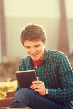 Genç adam tablet merdiven üstünde bir şehirde taping gülümseyen .