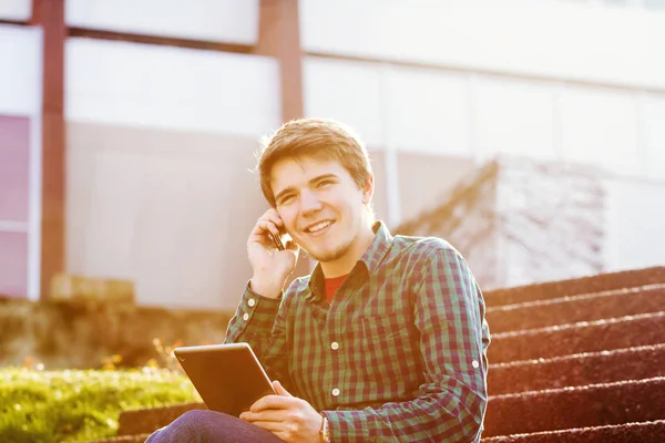 Souriant jeune homme tenant le livre et parlant sur un téléphone portable dans un — Photo