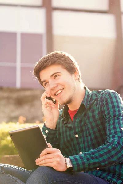 Souriant jeune homme tenant le livre et parlant sur un téléphone portable dans un — Photo