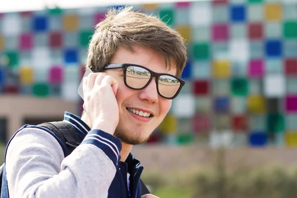 Un jeune homme souriant parle sur un téléphone portable dans une ville  . — Photo