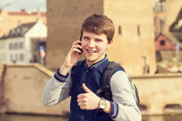 Un jeune homme souriant parle sur un téléphone portable dans une ville  . — Photo