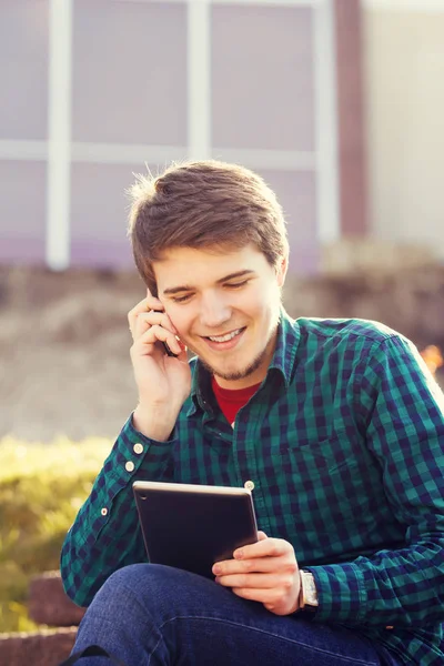 Un jeune homme souriant tenant un livre et parlant sur son téléphone portable — Photo