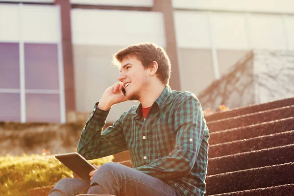 Un jeune homme souriant tenant un livre et parlant sur son téléphone portable — Photo