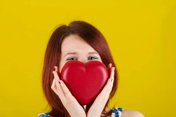 Woman showing holding  red heart. Love  concept with joyful young woman smiling isolated on yellow  background.