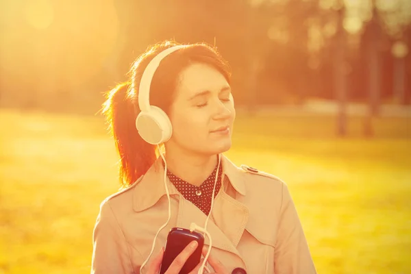 Woman listening to music in headphones in park  in sunlight in a sunny day