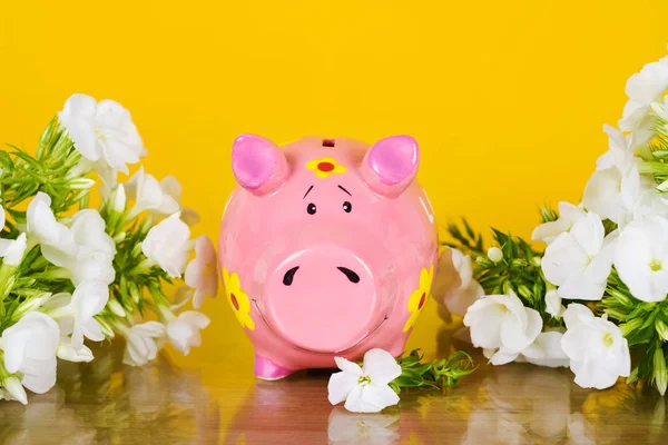 Piggy coin bank on yellow background with flowers — Stock Photo, Image