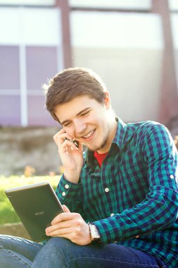 Tablet üzerinde kayıt ve merdiven üstünde bir şehirde cep telefonunda konuşma gülümseyen genç adam