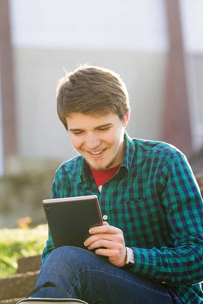 Un jeune homme souriant enregistre sur une tablette et parle sur un téléphone portable dans une ville par un escalier — Photo