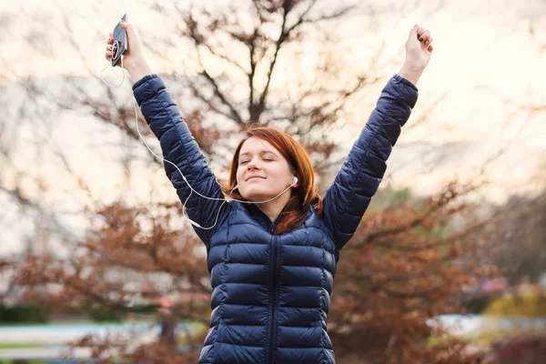 Mujer joven estirándose al aire libre en un parque de la ciudad escuchando música Fotos De Stock