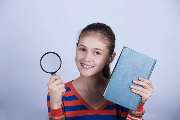 Sorrindo Retrato de uma linda colegial amando aprender com um livro e lupa , — Fotografia de Stock