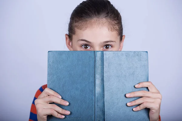 Little girl hiding herself behind book, studying, loving to learn