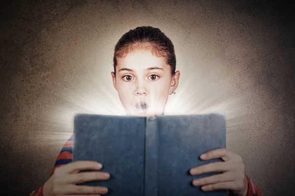 Överraskad, förvånad söt liten skolflicka med en öppen bok på hennes huvud — Stockfoto