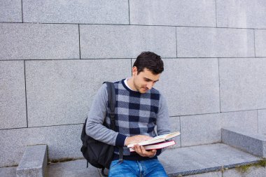 Bir kitap ve bir çanta Üniversitesi arka plan üzerinde tutan University.Smiling genç öğrenci adam