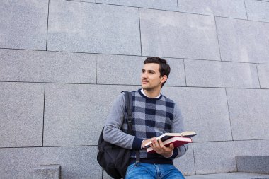 Bir kitap ve bir çanta Üniversitesi arka plan üzerinde tutan University.Smiling genç öğrenci adam 