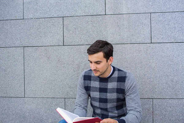 Jeune étudiant souriant tenant un livre et un sac sur fond universitaire — Photo