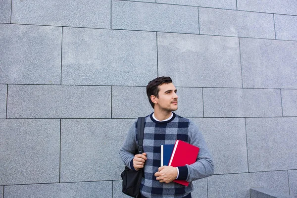 Un jeune étudiant souriant tenant un livre et un sac sur un fond universitaire — Photo