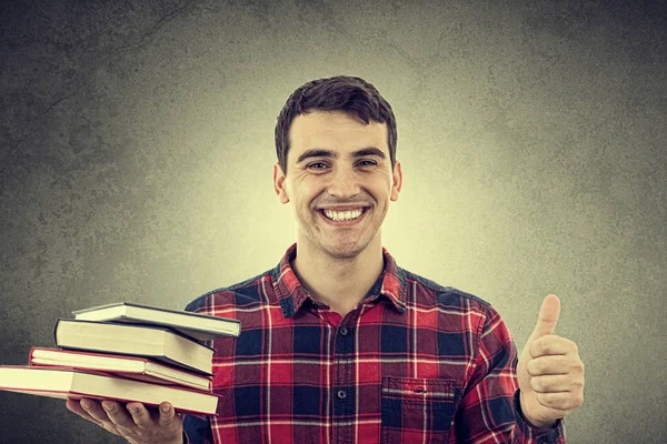 Étudiant souriant jeune homme avec le pouce levé tenant des livres sur sa main — Photo